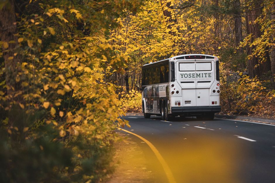 A charter bus driving along a scenic road through a national park with mountains in the background