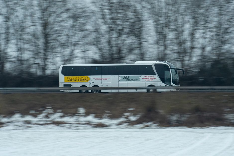 Charter bus parked at airport pickup zone with passengers loading luggage