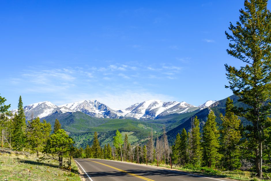 Charter bus driving along a scenic mountain highway in Colorado with alpine peaks in the background